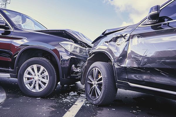 Two black SUVs collided head-on, with significant front-end damage; debris on the pavement.