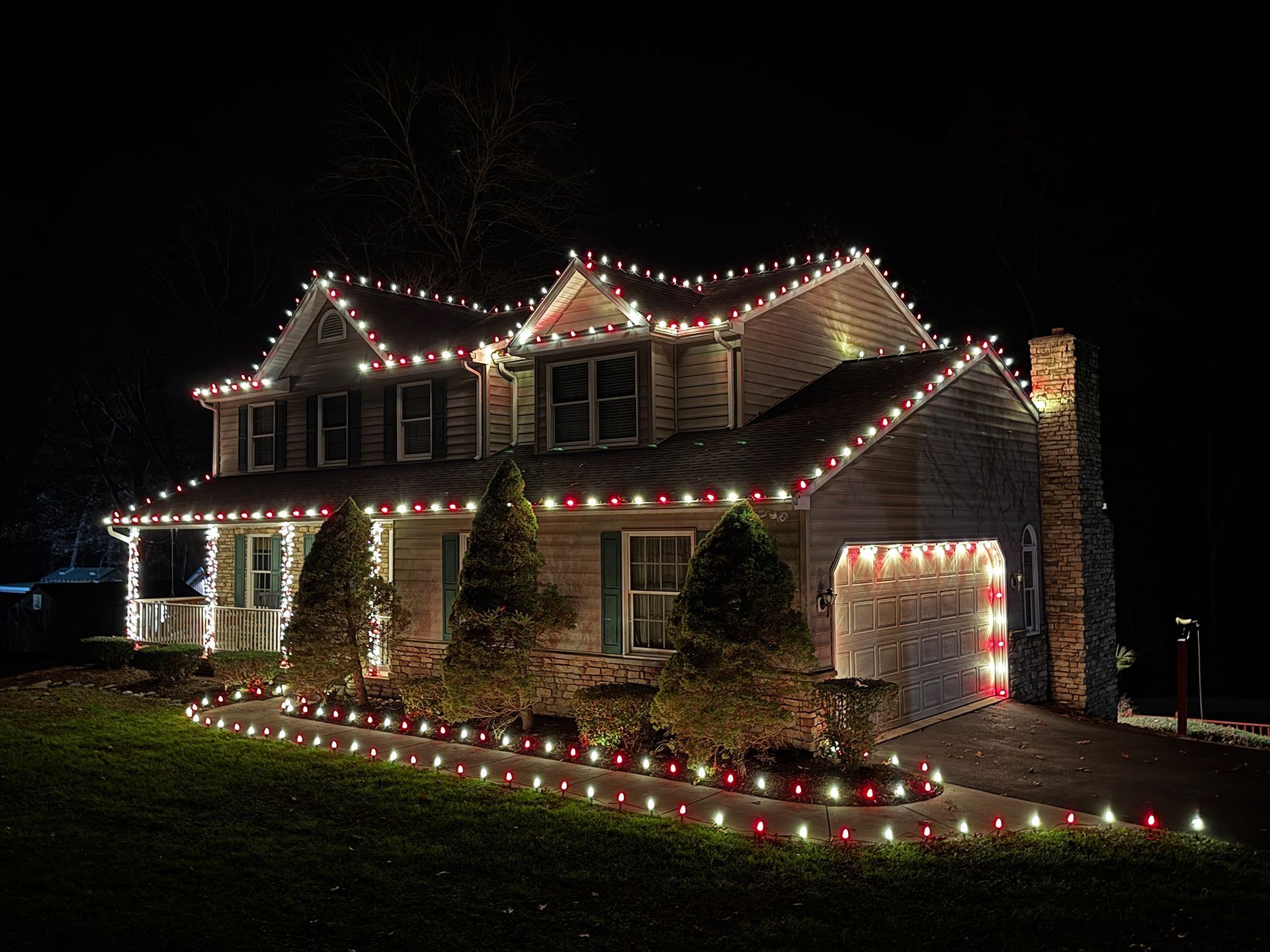 The house is decorated with red and white Christmas lights at night.