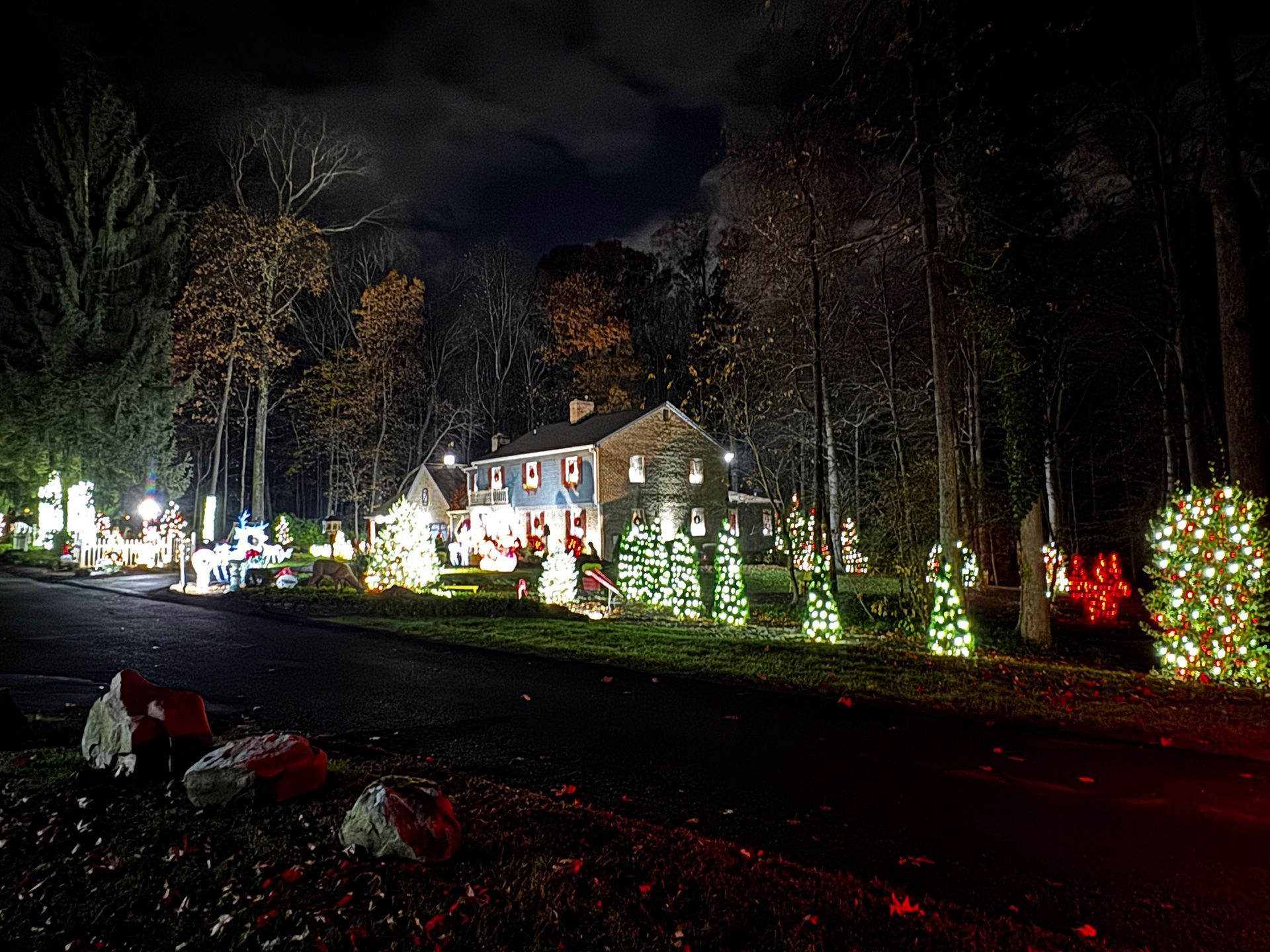 The house is decorated with Christmas lights at night, and trees line the road.