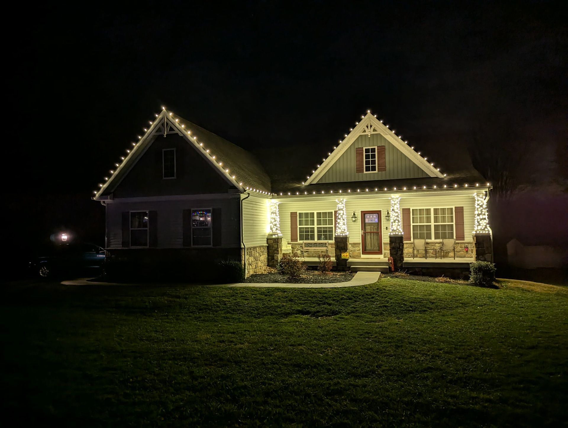 House at night with roof and porch outlined in warm white Christmas lights.