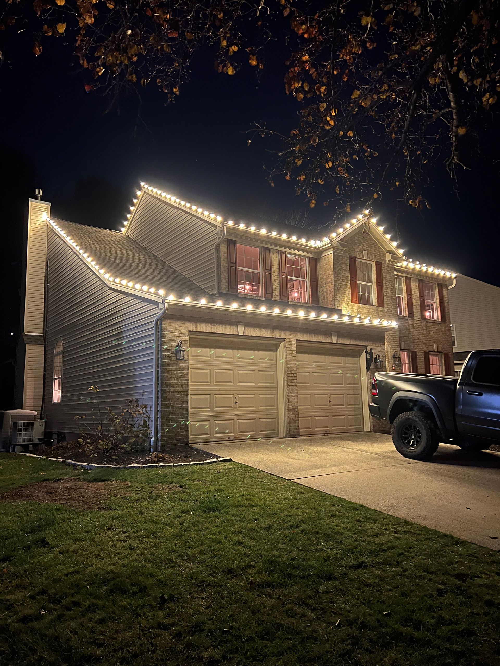 House at night with roofline Christmas lights. Garage, driveway, truck parked, and dark sky.
