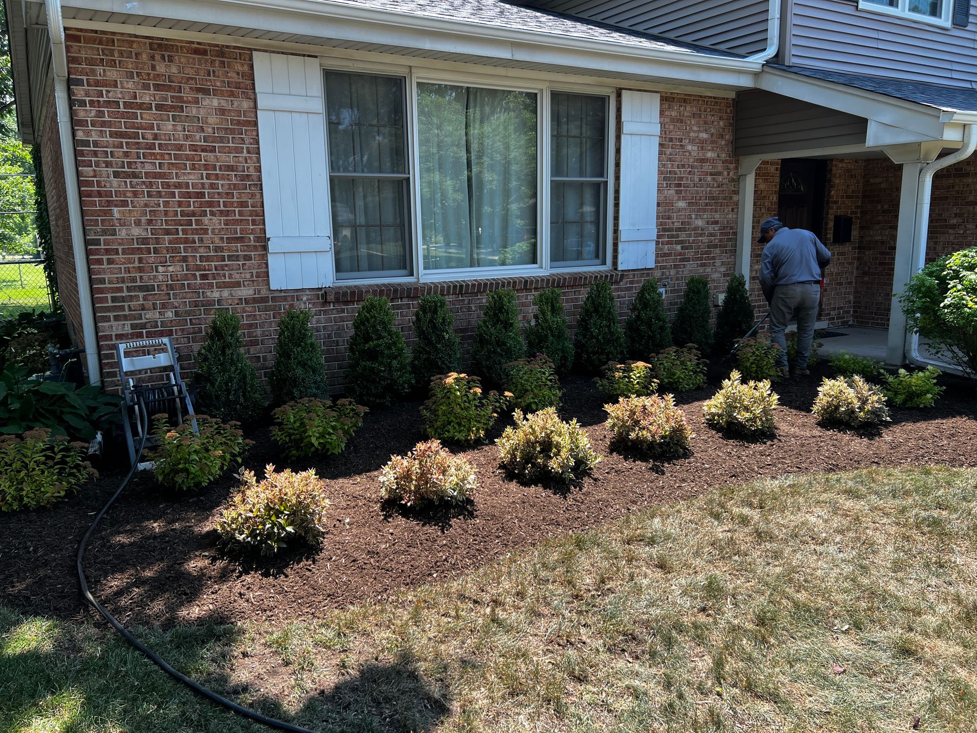Landscaped front yard with shrubs and a person near the front porch of a brick house