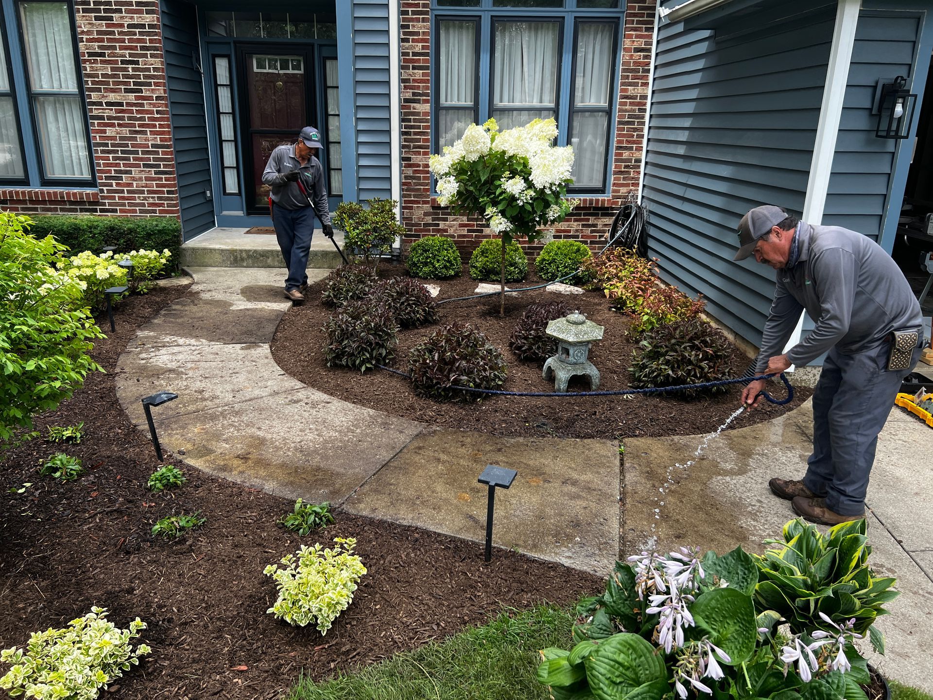Two people landscaping a curved brick patio garden beside a house