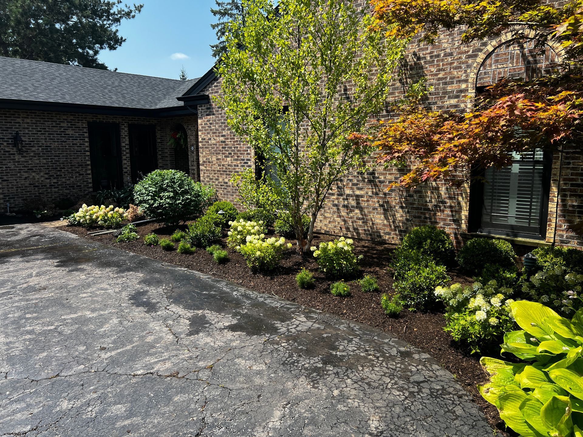 Courtyard with stone wall, curved roof, and lush green landscaping beside a paved drive