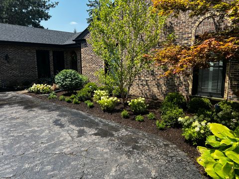 Courtyard with stone wall, curved roof, and lush green landscaping beside a paved drive