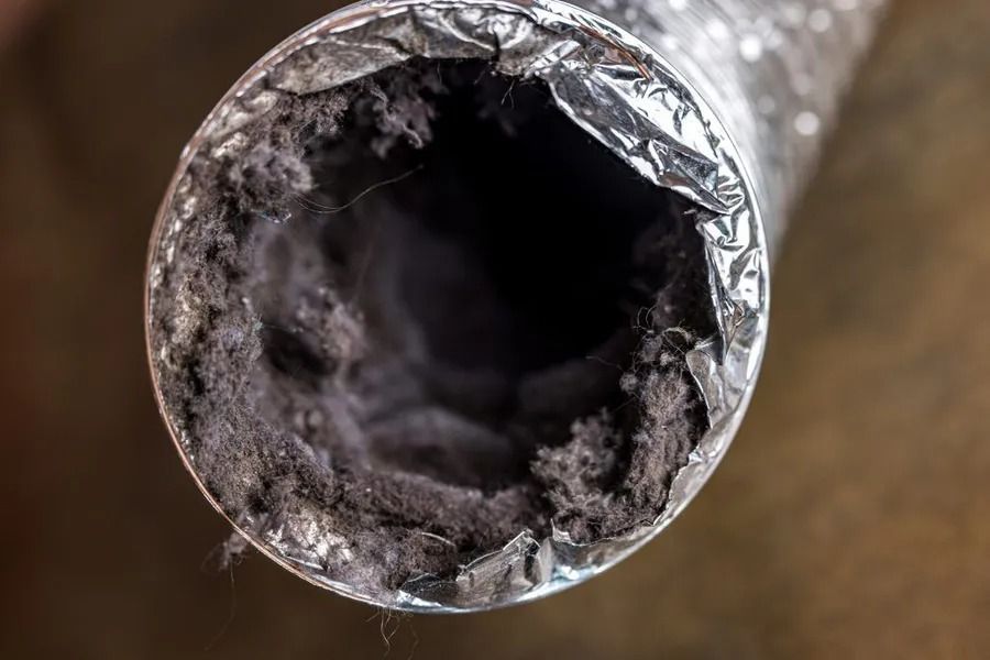 Close-up of a dryer vent tube clogged with thick, dark gray lint.