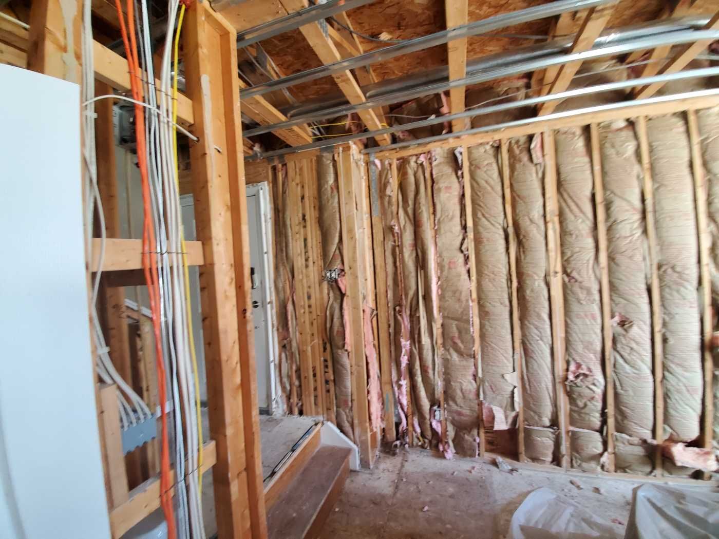 Interior wall under construction with exposed insulation, framing, and wiring.