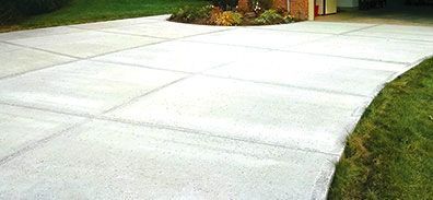 A concrete driveway leading to a house with a brick building in the background.