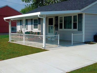 A white house with a porch and a red barn in the background.