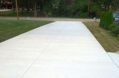 A concrete driveway leading to a house with trees in the background.