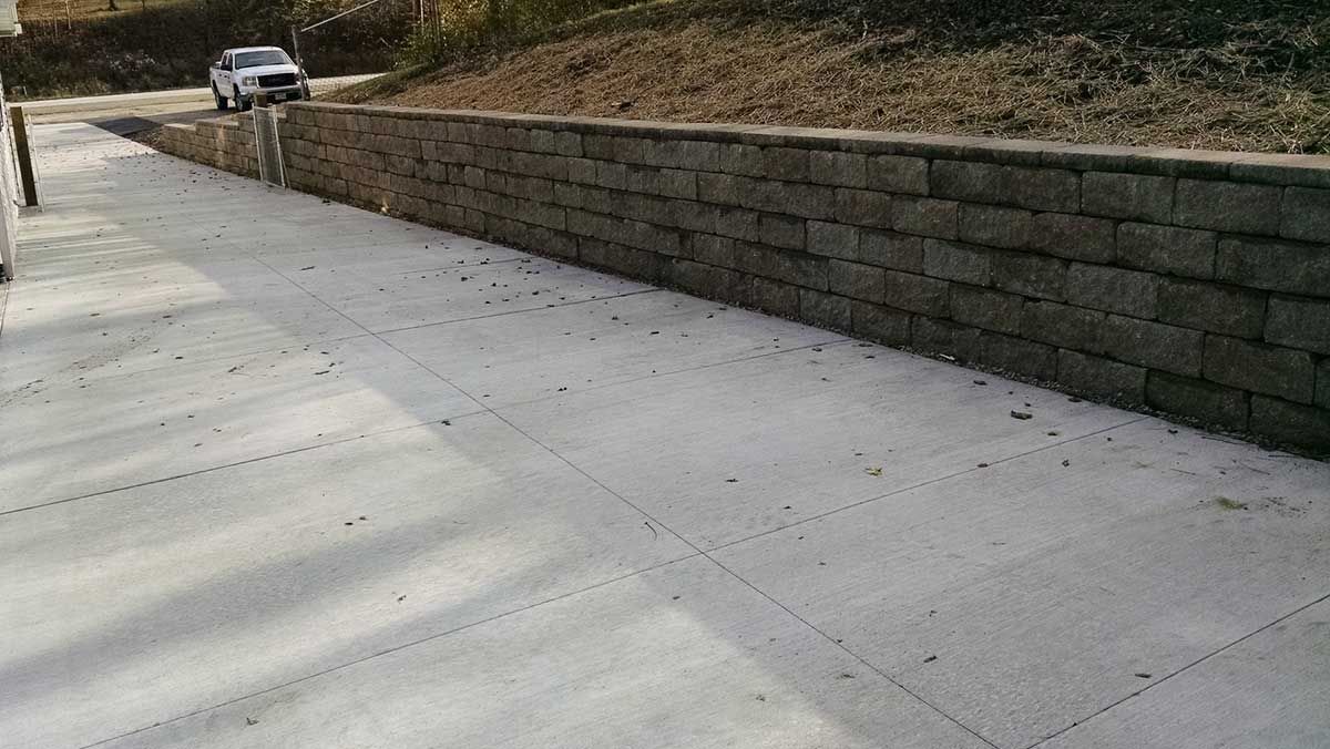 A car is driving down a concrete driveway next to a brick wall.