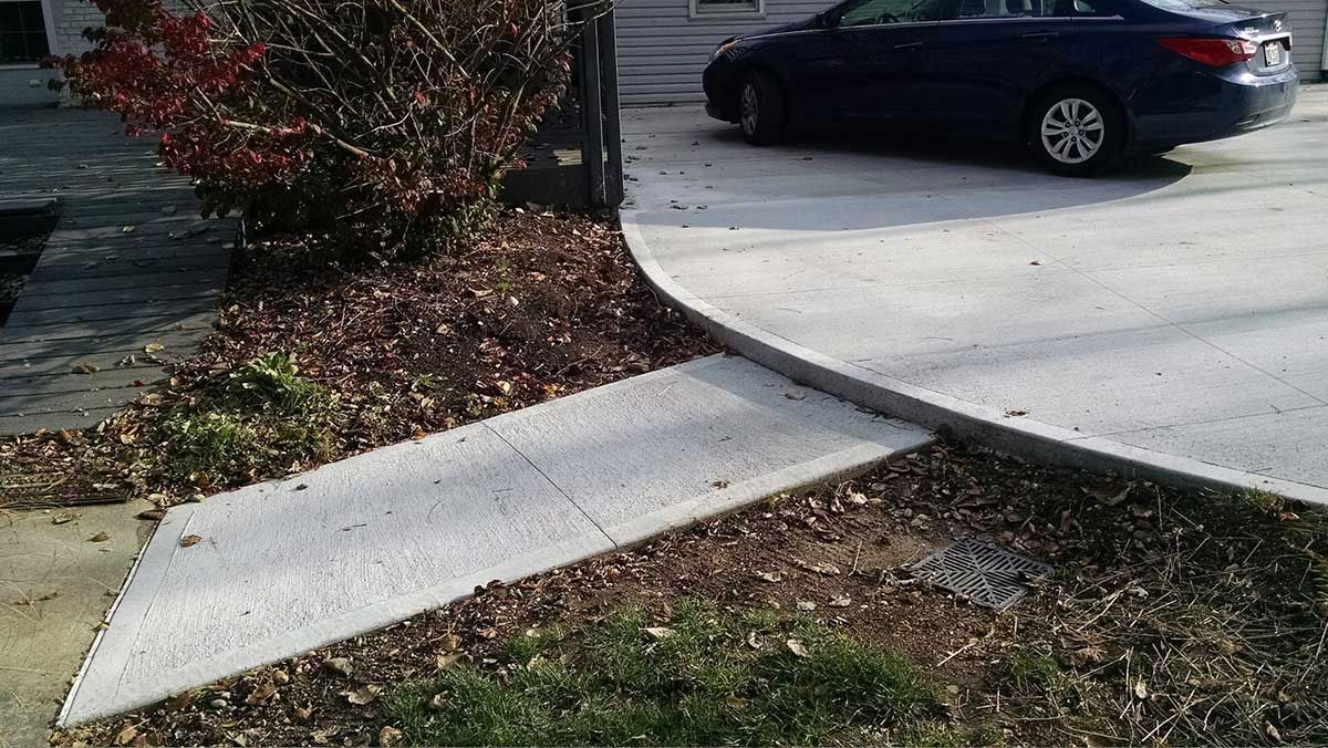 A car is parked in a driveway next to a sidewalk.