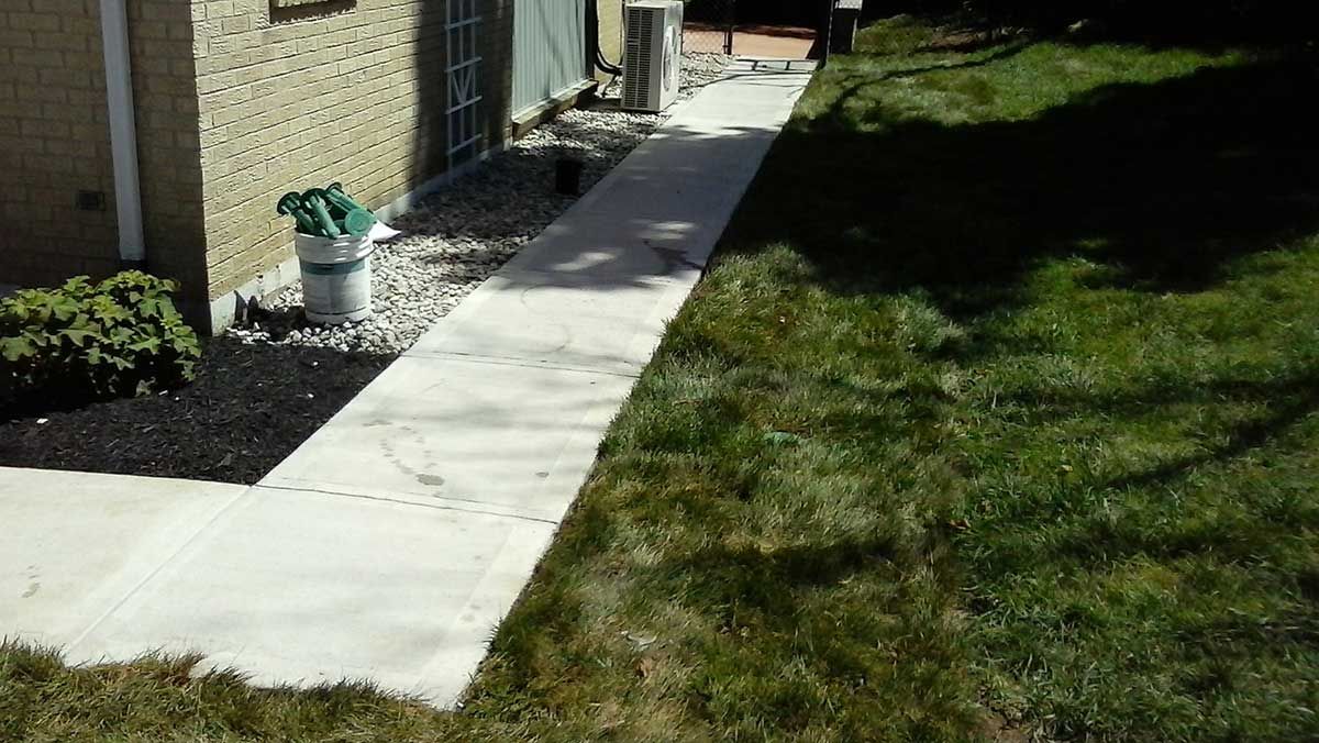 A concrete walkway leading to a house in a backyard.