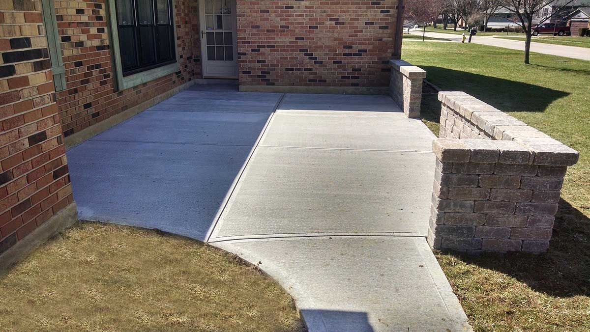 A brick house with a concrete walkway leading to it.