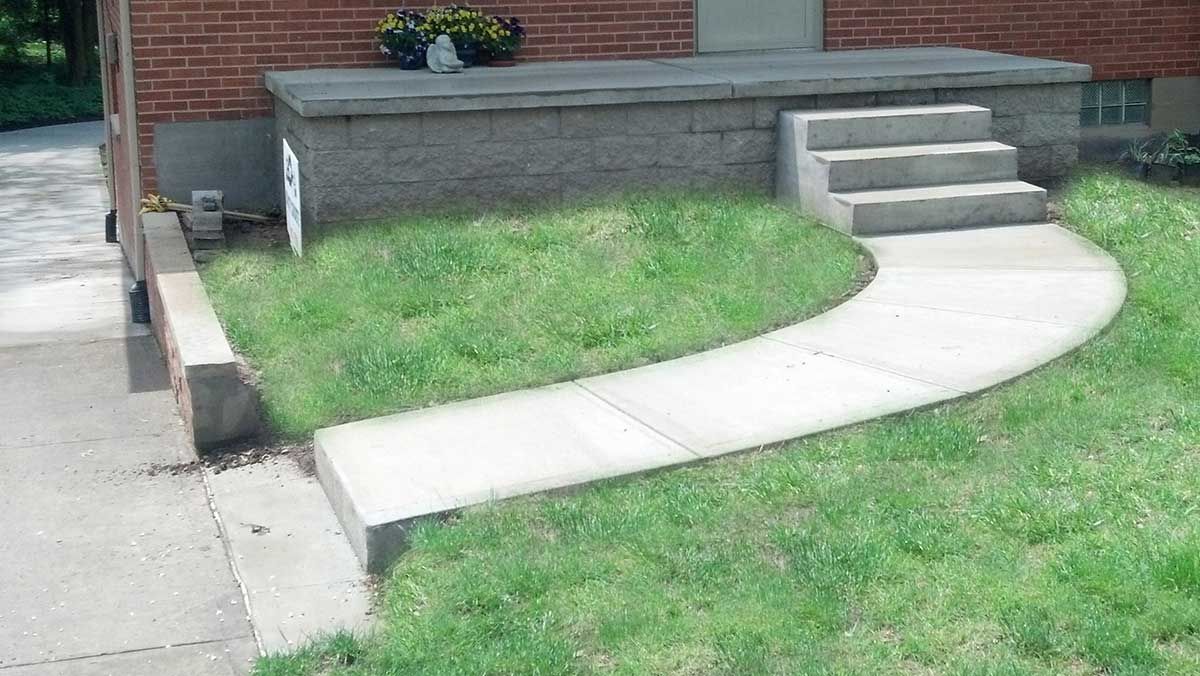 A concrete walkway with steps leading to a porch in front of a brick house.