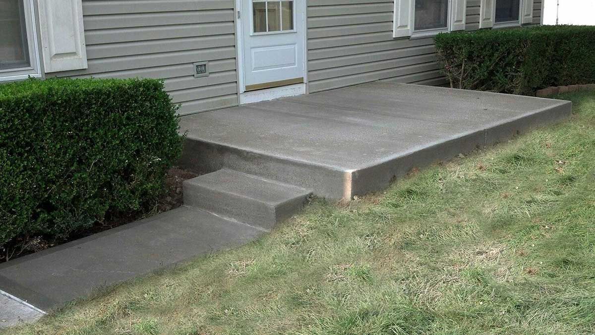 A concrete porch with steps leading to the front door of a house.