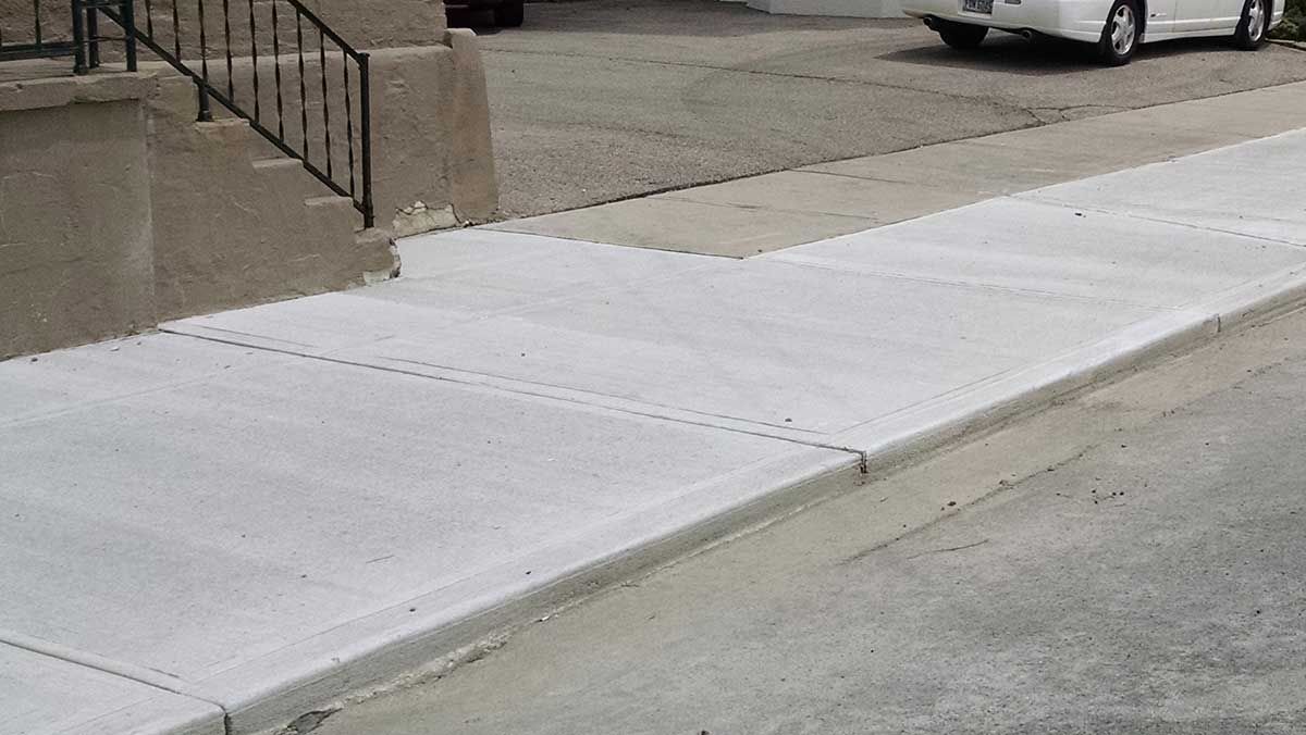 A white car is parked on the side of the road next to a sidewalk.