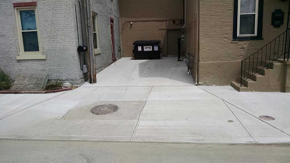 A concrete driveway leading to a brick building with stairs.