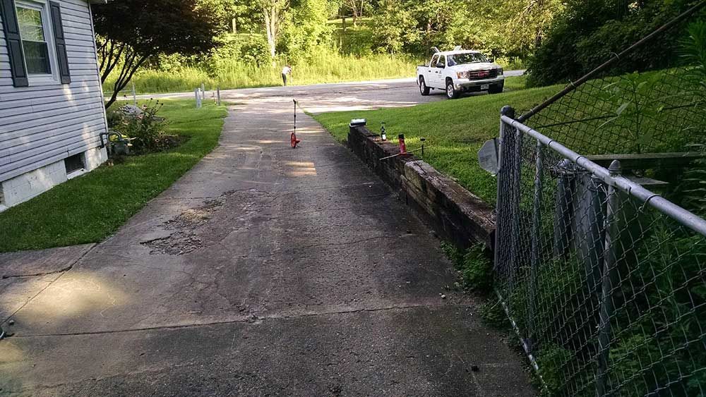 A white truck is parked on the side of a driveway next to a chain link fence.