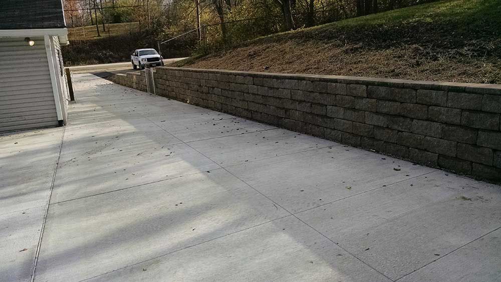 A car is driving down a concrete driveway next to a brick wall.