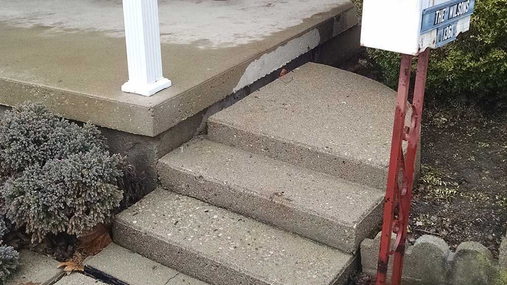 A set of concrete steps leading up to a porch next to a mailbox.