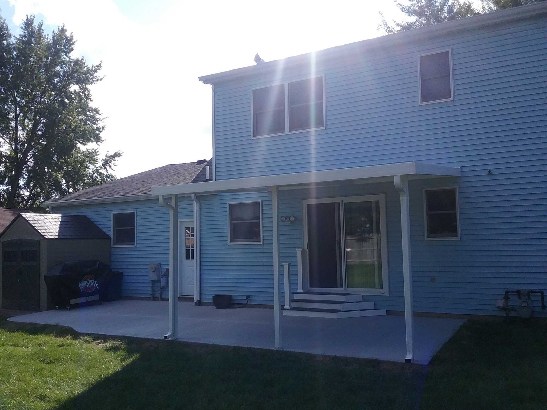 A blue house with a white porch and a shed in the backyard.