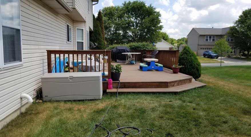 There is a deck with a table and chairs on it in the backyard of a house.