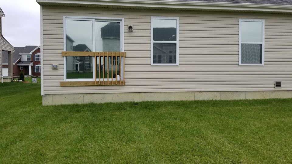 The back of a mobile home with a deck and sliding glass doors.
