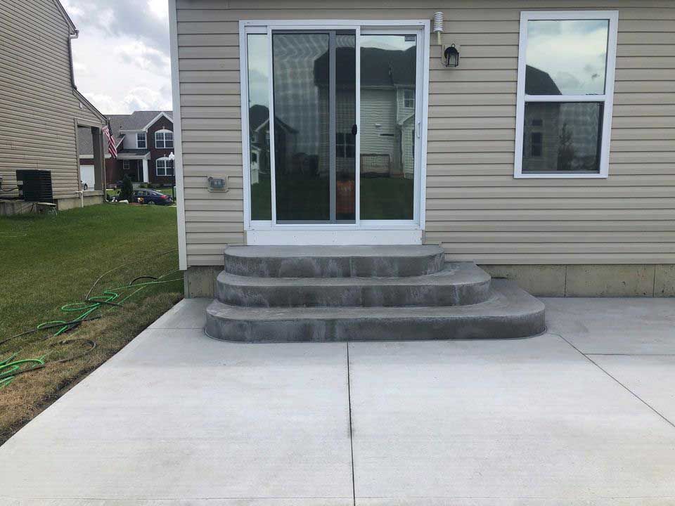 A house with a sliding glass door and concrete steps leading to it.