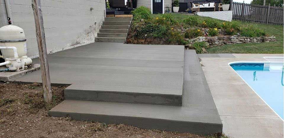 A concrete deck with stairs leading up to a swimming pool.