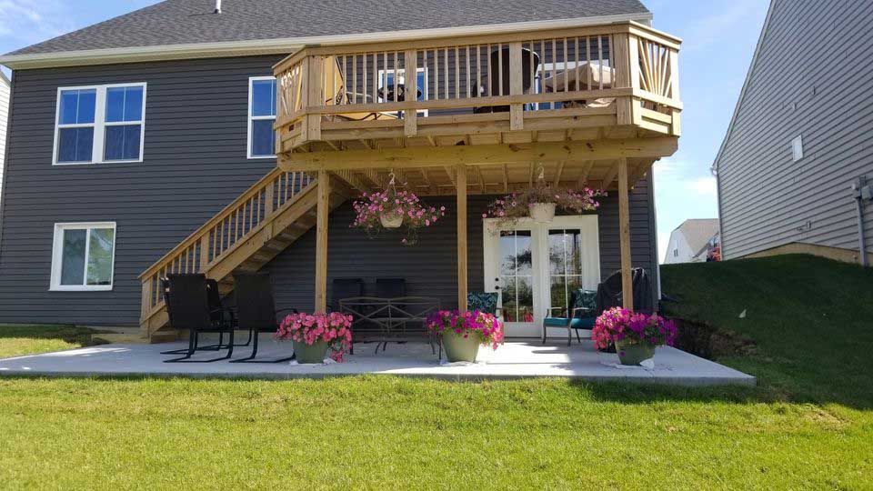 A large wooden deck with stairs leading up to it is in the backyard of a house.