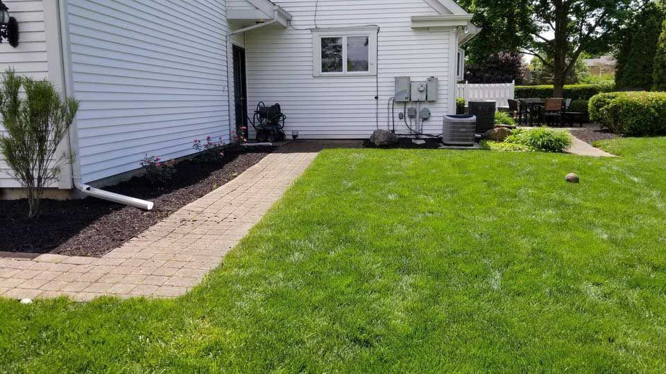 A white house with a lush green lawn and a brick walkway leading to it.