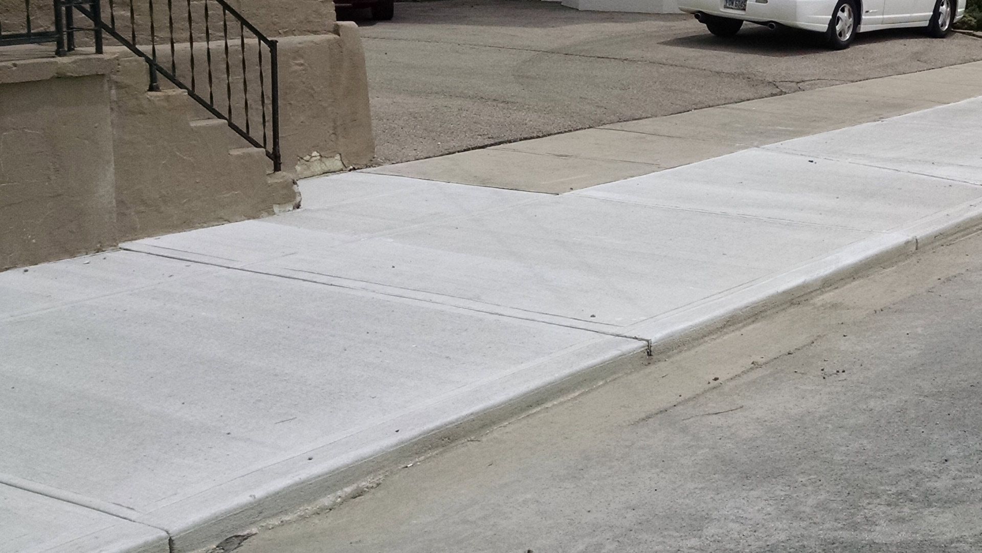 A white car is parked on the side of the road next to a sidewalk.