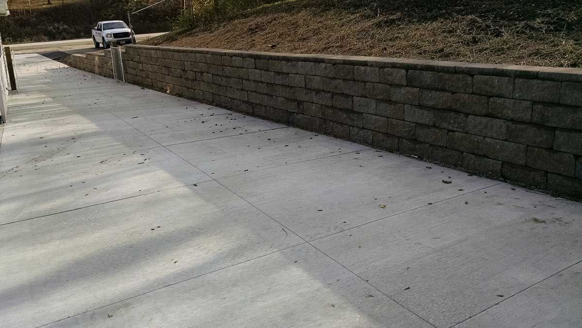 A car is driving down a concrete driveway next to a brick wall.
