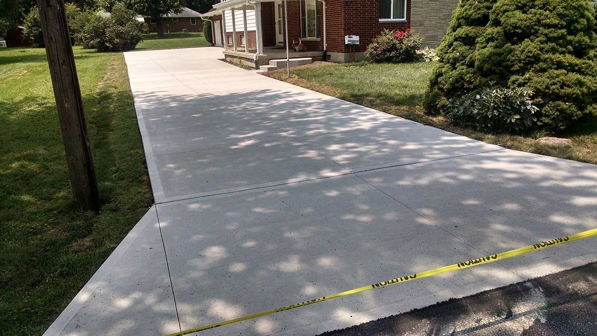 A concrete driveway leading to a house with a yellow tape.