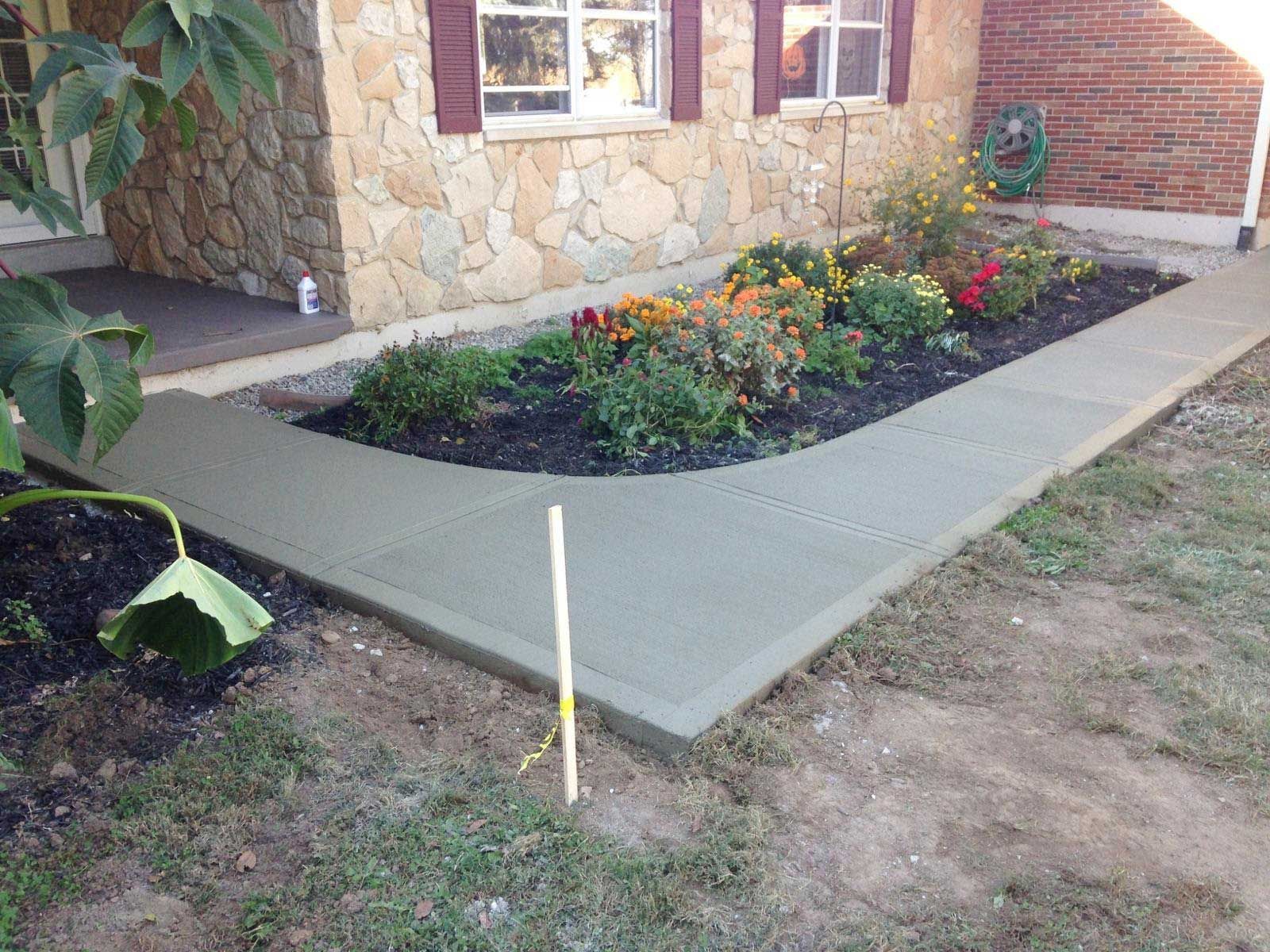 A concrete walkway is being built in front of a brick house.