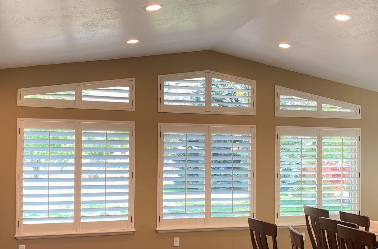 Three windows with white shutters in a tan-walled room, with two triangular windows above.