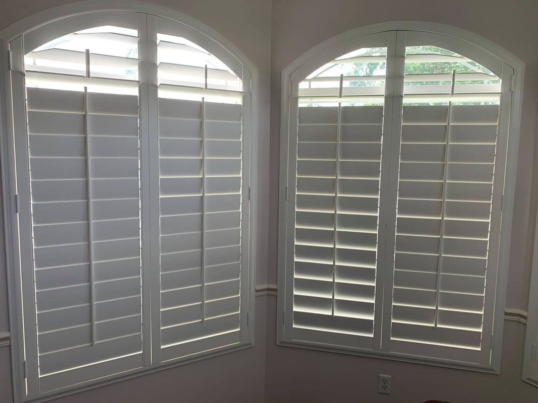 Two white arched windows with white shutters, in an interior room.