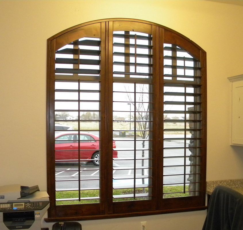 Wooden window with arched top, three panes, shuttered, looking onto a parking lot and red car.