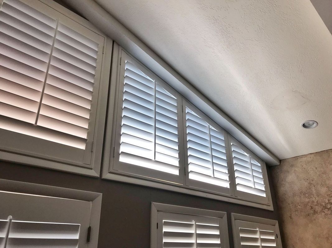 White shutters on a wall with angled windows. Some shutters are open, others are closed, letting in light.