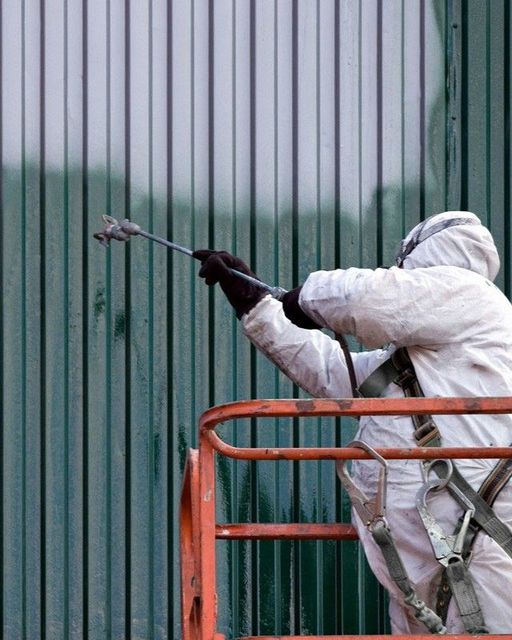 A man in a protective suit is spraying paint on a green wall.