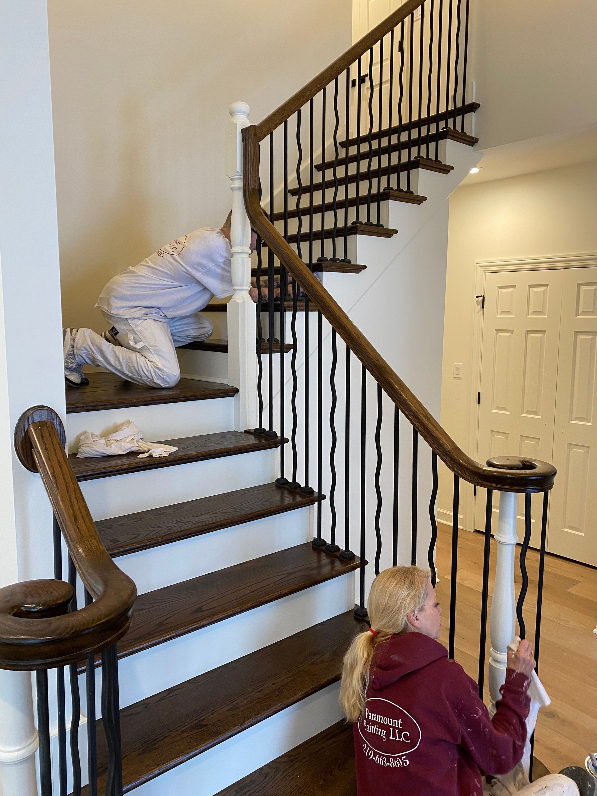 A woman is kneeling on the floor next to a staircase.