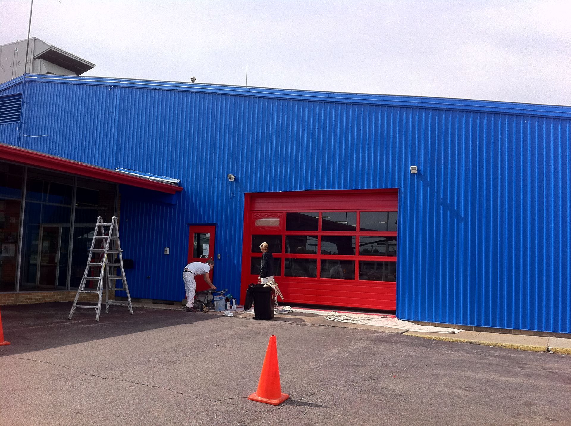 A blue building with a red garage door is being painted