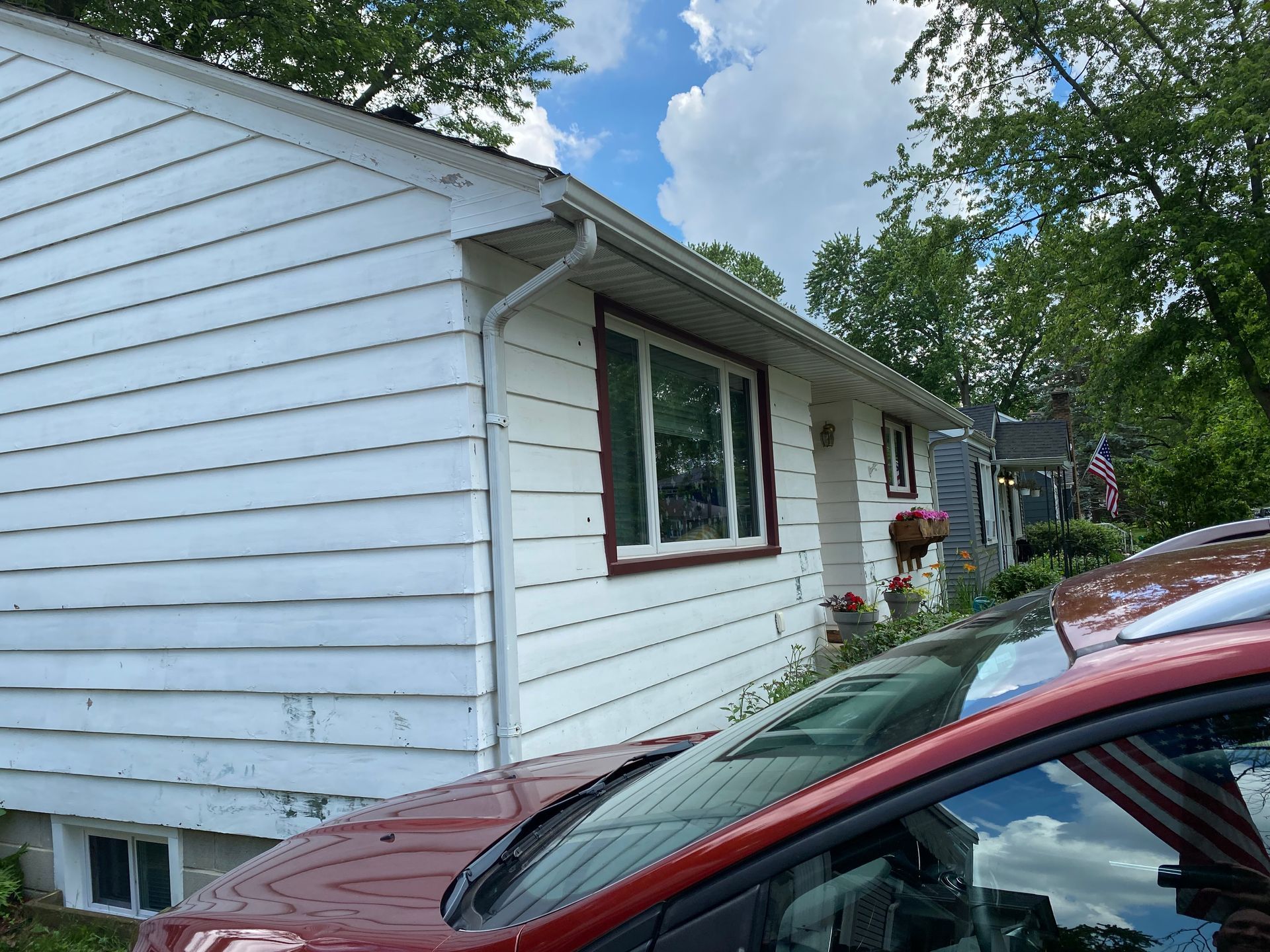 A red car is parked in front of a white house.