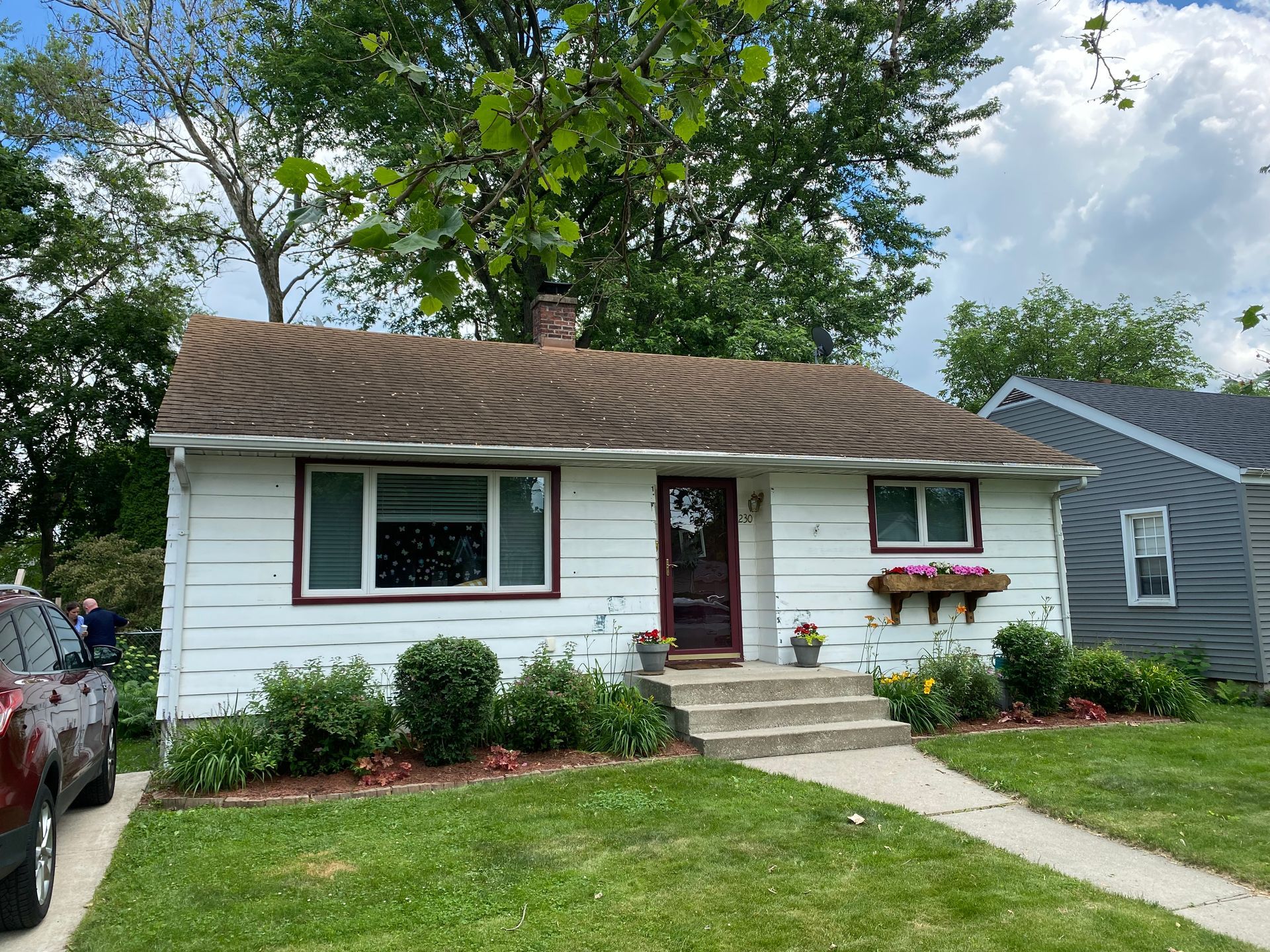 A white house with a brown roof and a car parked in front of it.
