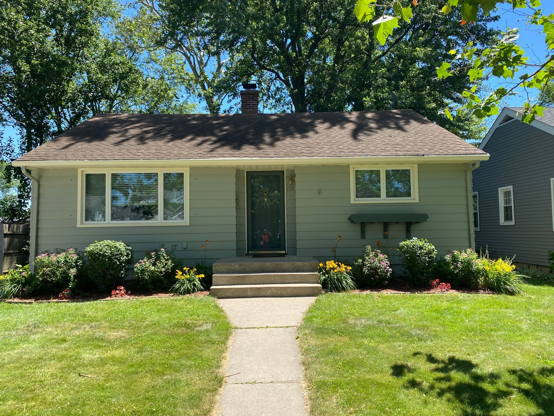 A gray house with a brown roof is sitting on top of a lush green lawn.