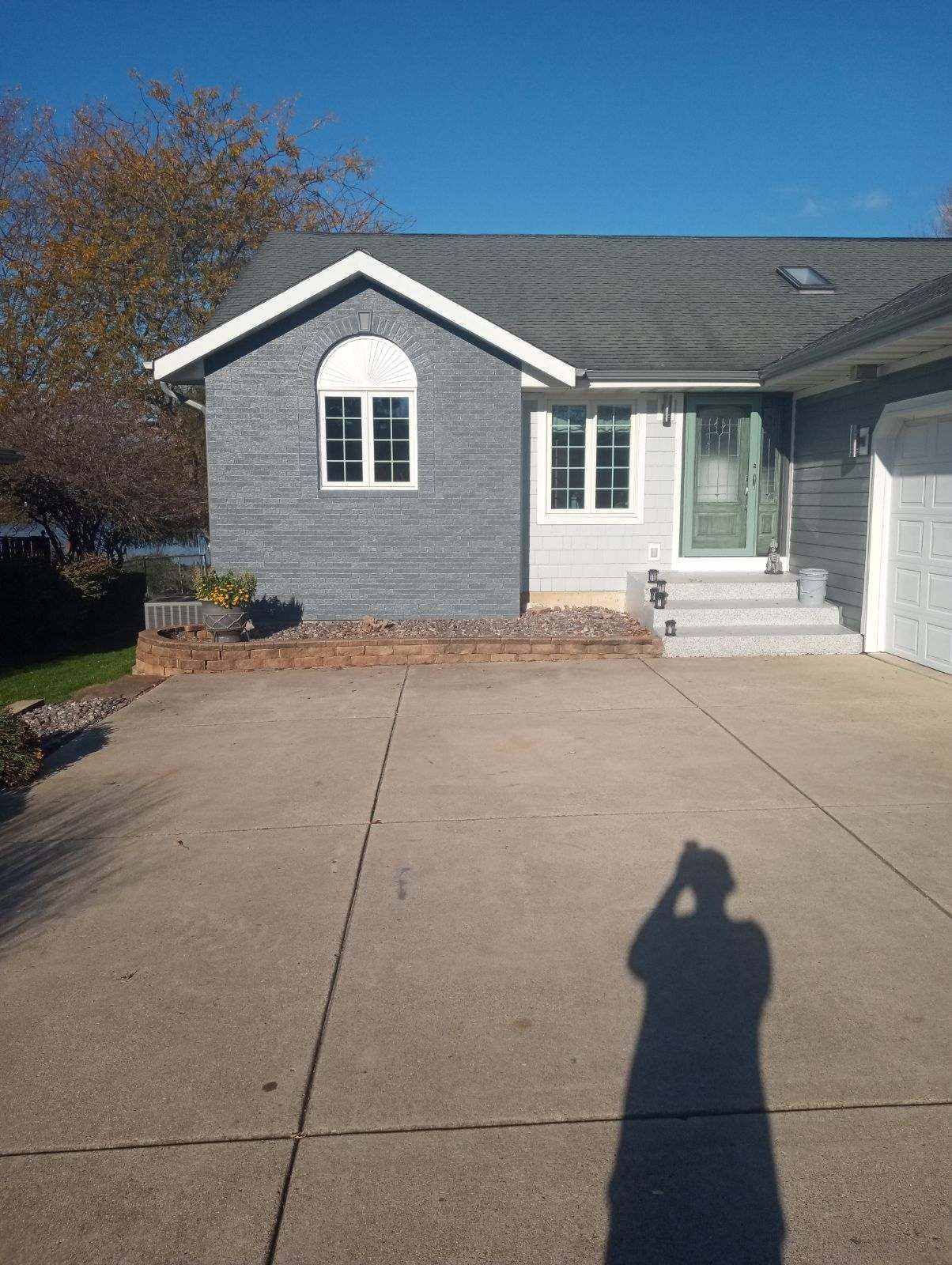 A shadow of a person is cast on the driveway of a house.