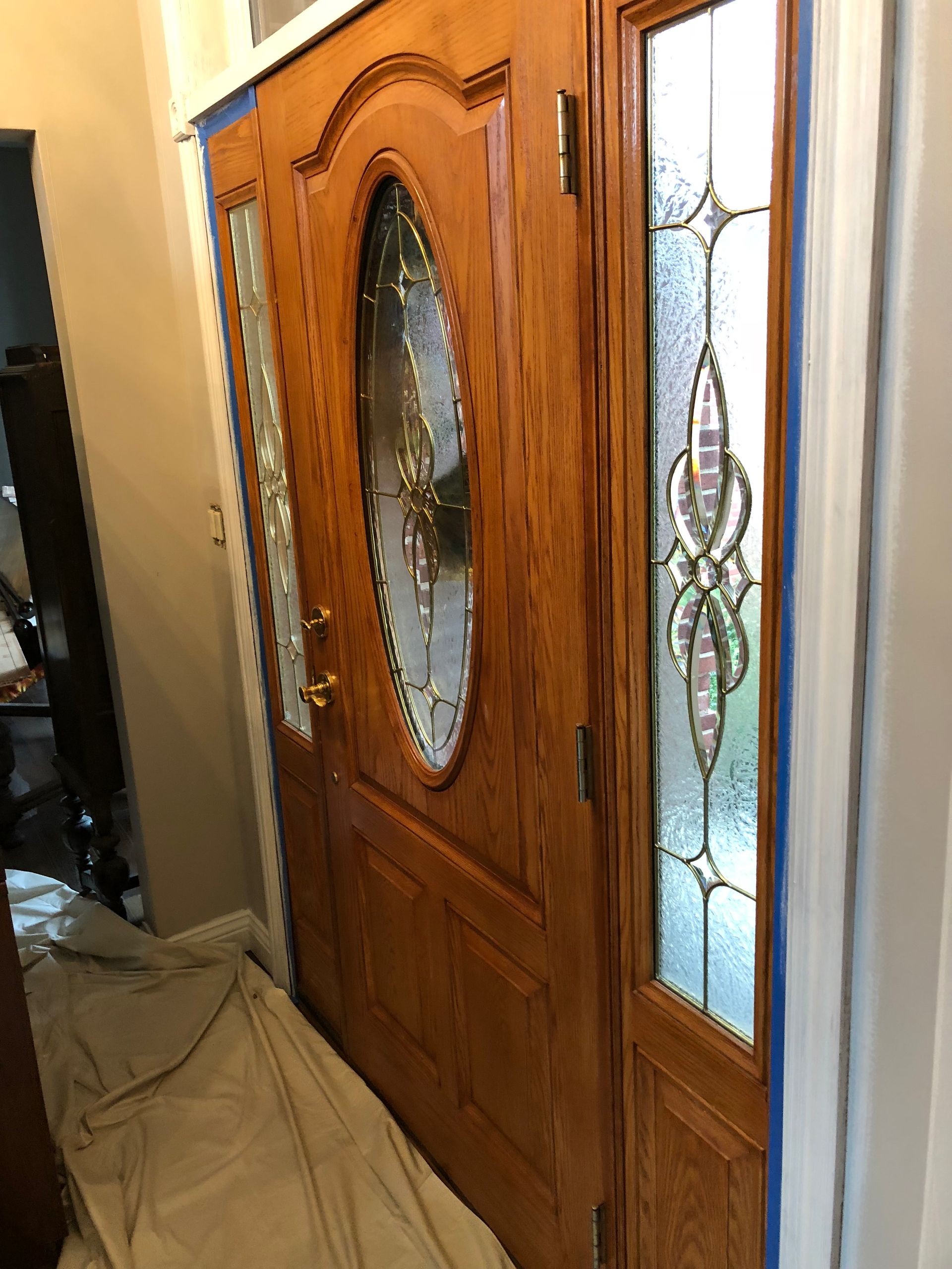A wooden door with a stained glass window is being painted in a hallway.