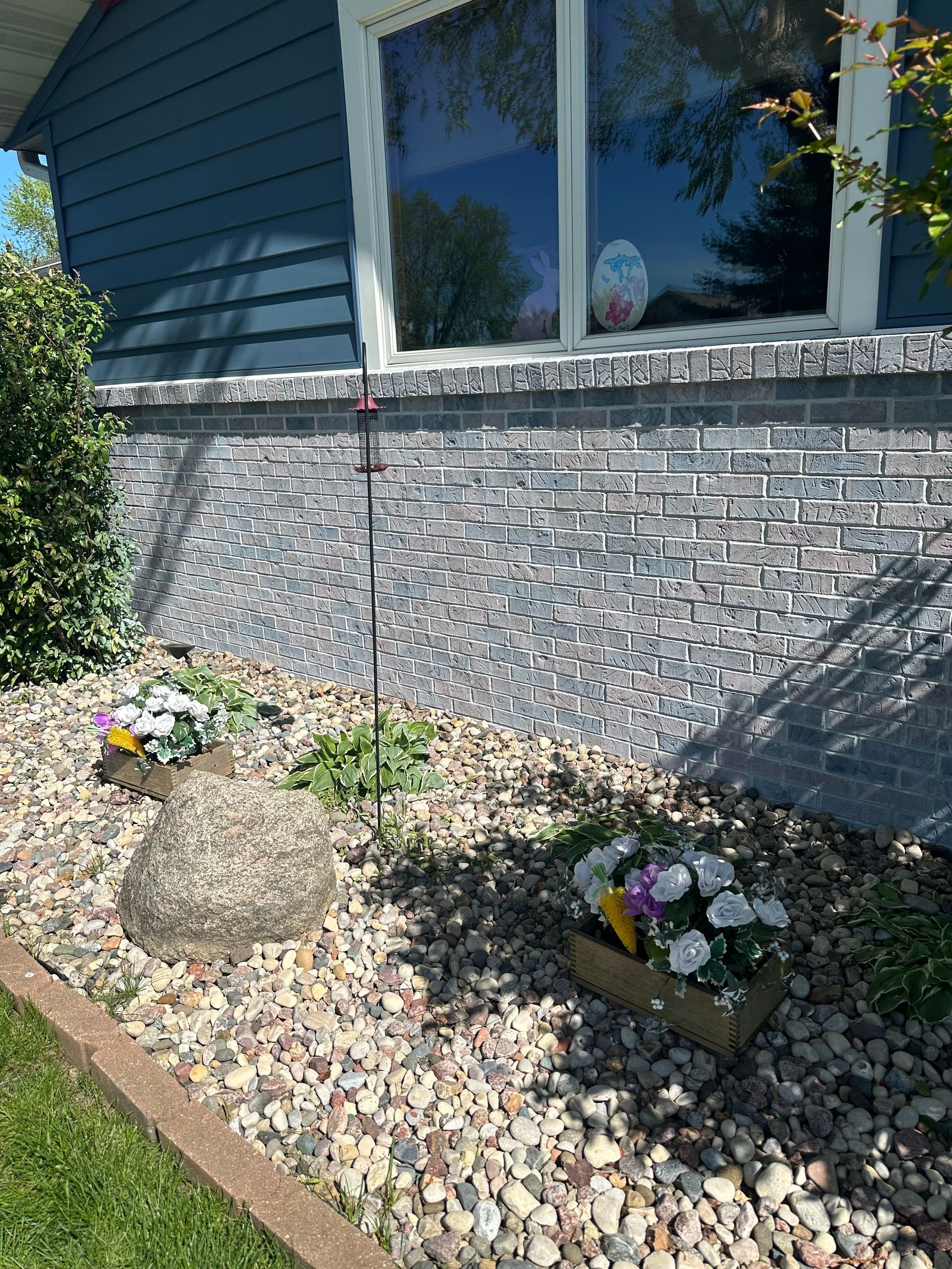 A house with a brick wall and a rock garden in front of it.