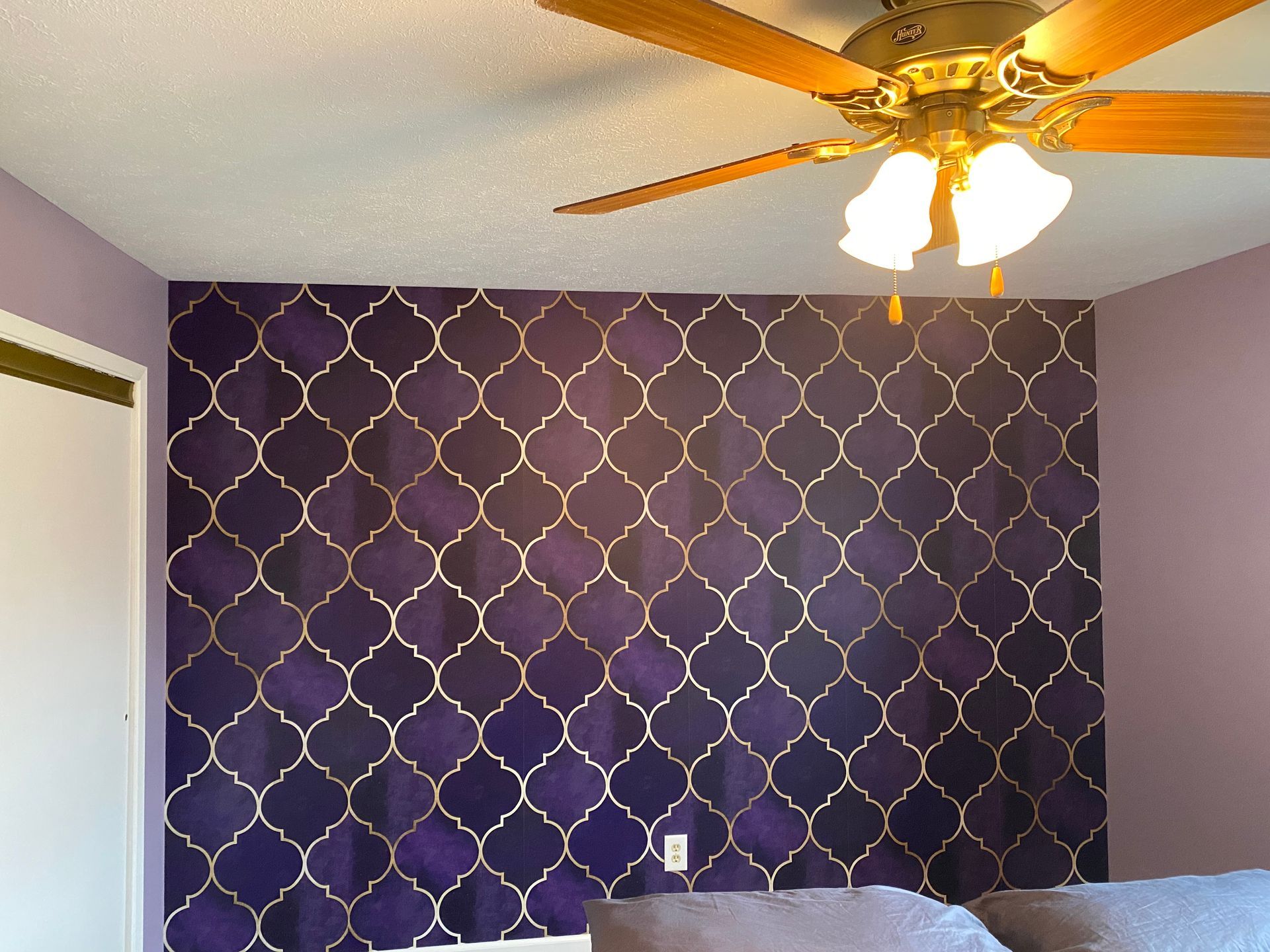 A bedroom with a purple wall and a ceiling fan